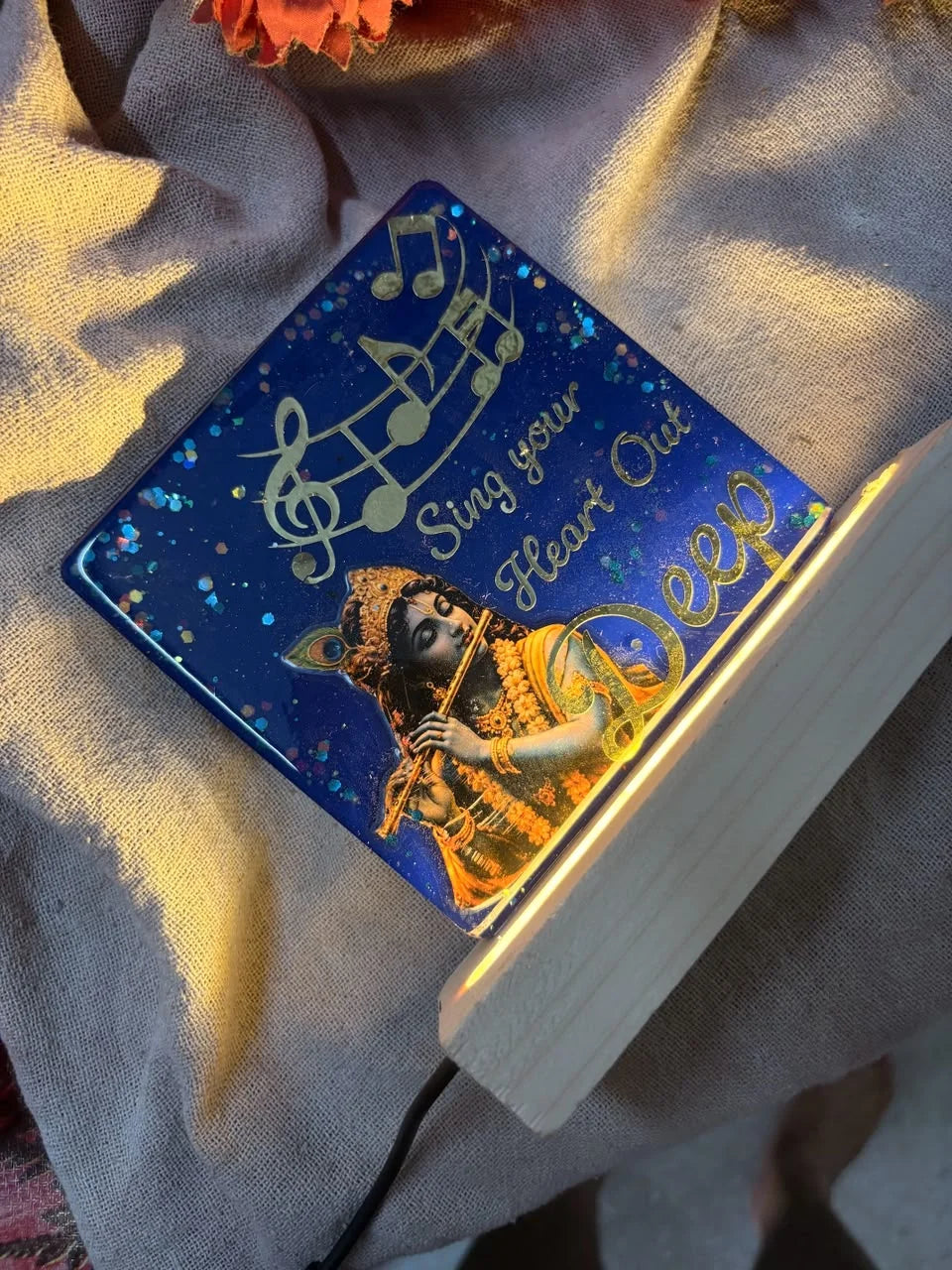 Blue resin keepsake featuring Krishna playing flute, golden musical notes, and 'Sing your Heart Out,' illuminated by a wooden