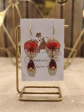A pair of handcrafted gold-tone drop earrings featuring circular clear resin with preserved red flowers and deep red teardrop
