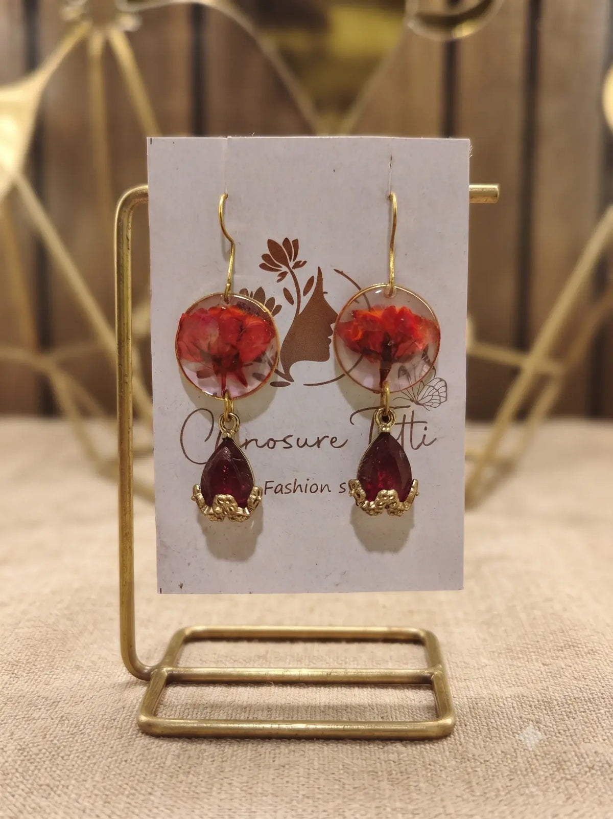 A pair of handcrafted gold-tone drop earrings featuring circular clear resin with preserved red flowers and deep red teardrop