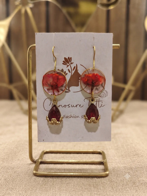 A pair of handcrafted gold-tone drop earrings featuring circular clear resin with preserved red flowers and deep red teardrop