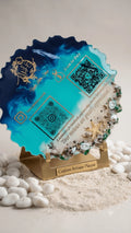 Custom resin QR code plaque with blue, teal, and white swirls, decorated with seashells and starfish, on a gold stand.