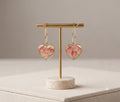 Pair of gold-toned heart-shaped hoop earrings with pink dried rose petals and gold flakes encased in clear resin, displayed o