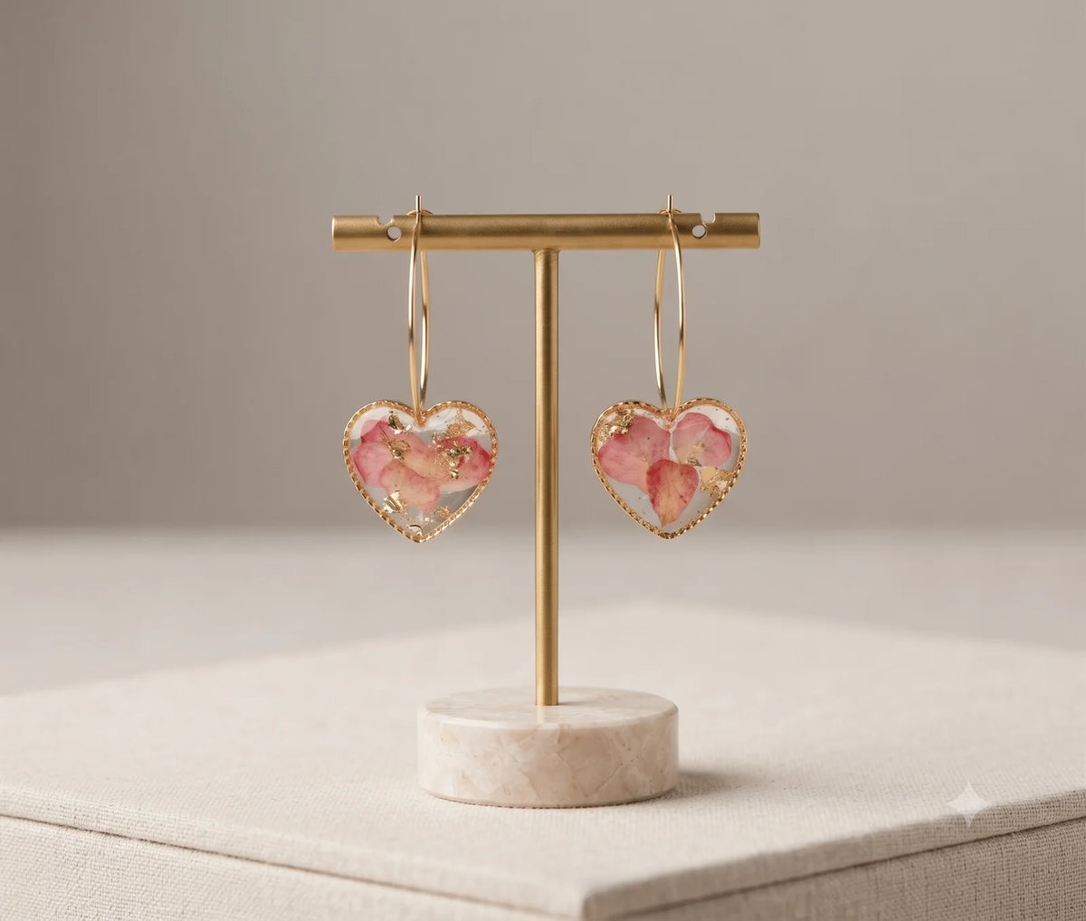 Pair of gold-toned heart-shaped hoop earrings with pink dried rose petals and gold flakes encased in clear resin, displayed o