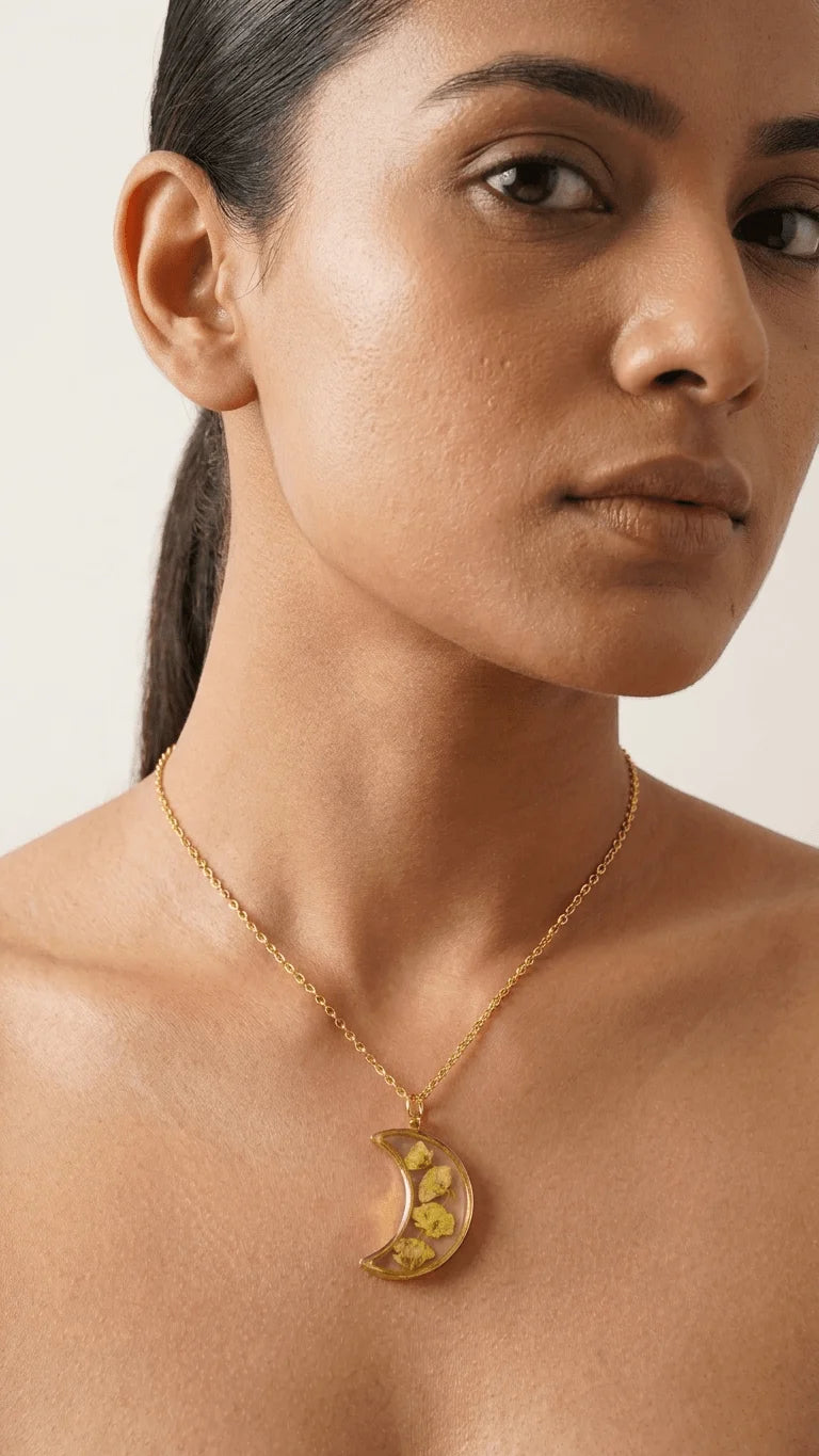 Woman wearing a gold chain with a crescent moon resin pendant featuring yellow dried flowers.