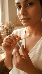 Woman holding a gold chain necklace with a round resin pendant featuring pressed dark green flowers.