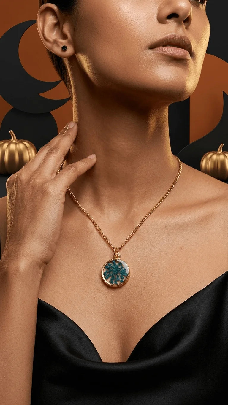 A person in a black dress wears a gold chain with a teal resin floral pendant, against an orange and black background with go
