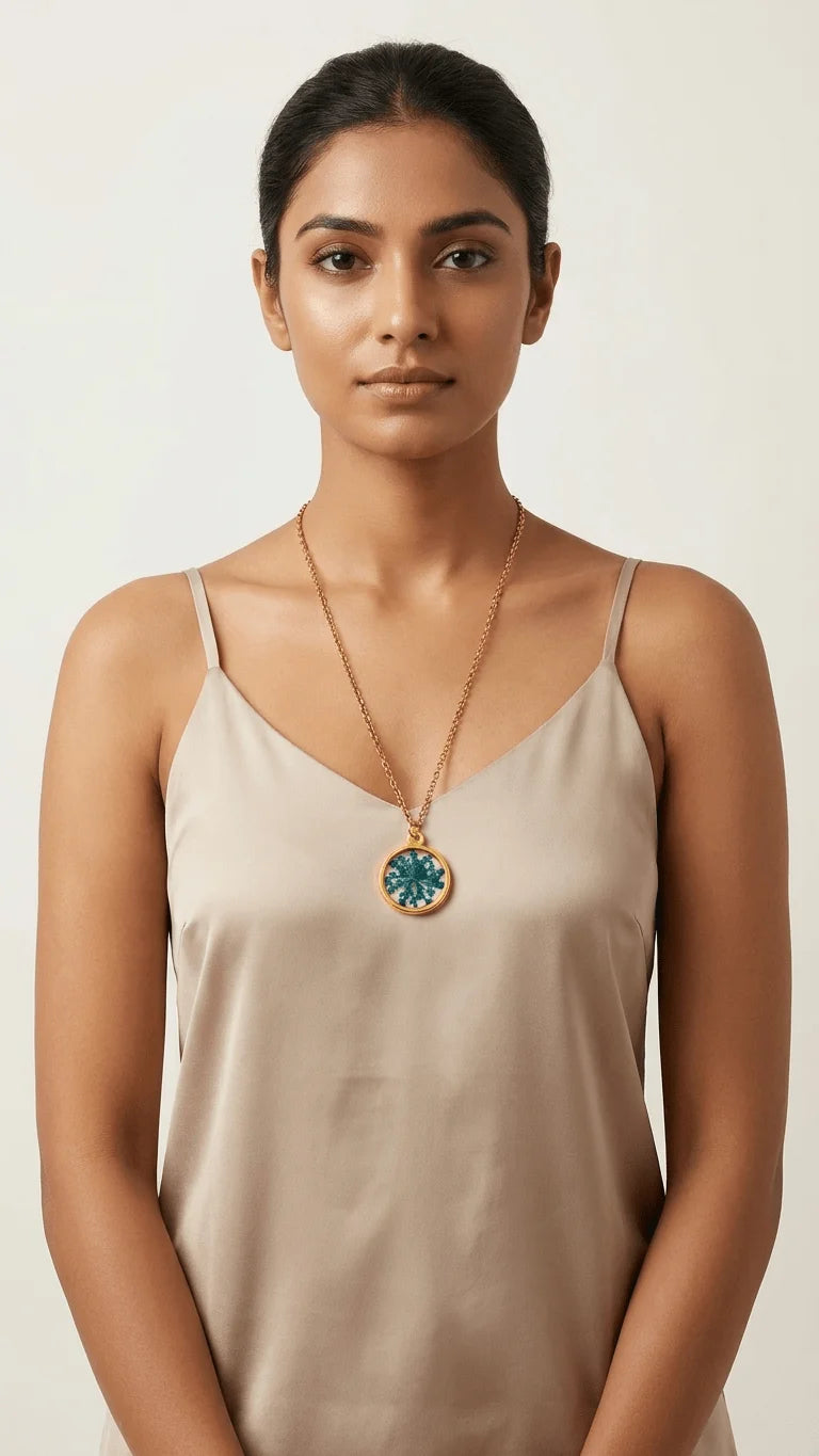 Woman wearing a beige camisole and a long gold chain with a round teal and white patterned resin pendant.