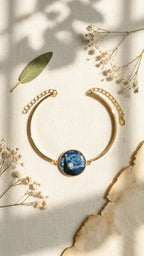 Gold-tone cuff bracelet featuring a circular resin charm with Van Gogh's Starry Night painting, on a light fabric background.