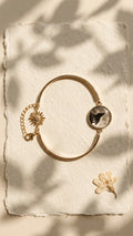 Gold-tone bangle bracelet with a round resin charm featuring a black howling wolf silhouette against a moon, and a sun charm,