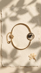 Gold-tone bangle bracelet with a round resin charm featuring a black howling wolf silhouette against a moon, and a sun charm,
