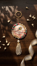 Handcrafted round resin keychain with 'Krishna Sahayate' calligraphy, peacock feather, gold accents, floral border, and pearl