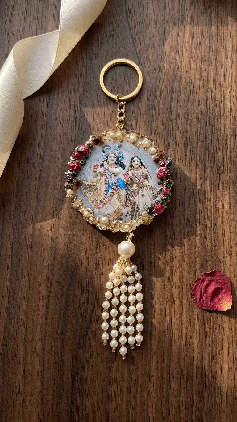 Round resin keychain featuring Radha Krishna, surrounded by pearls and red floral accents, with a pearl tassel, on a wooden s