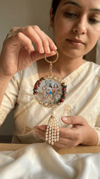 Handcrafted resin keepsake with Radha Krishna image, pearl border, and pearl tassel, held by a woman in a cream outfit.
