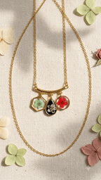 Gold chain necklace with three resin pendants, each featuring a pressed flower, displayed on a neutral fabric background.