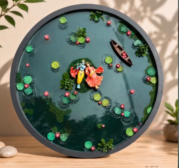 Circular resin art piece depicting Radha and Krishna standing on an island in a pond with lotus leaves, pink flowers, and a s