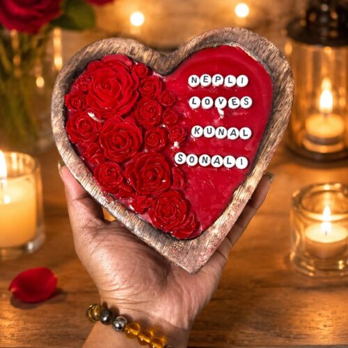 Hand holding a heart-shaped wooden tray with red resin roses and names 'NEPLI LOVES KUNAL SONALI' in a warm, candlelit settin
