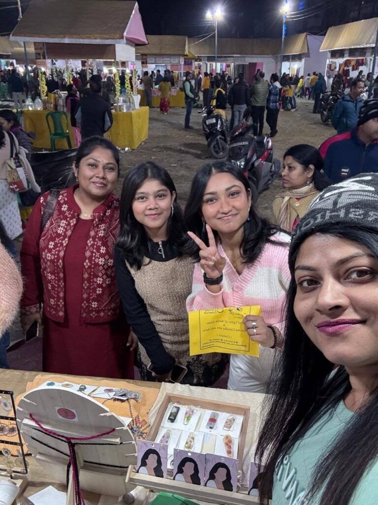 Four smiling women at a night market stall displaying handmade resin jewelry and keepsakes.