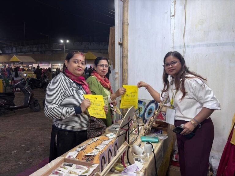Three women at a bustling night market stall, two holding yellow bags, while the third stands behind a display of handmade re