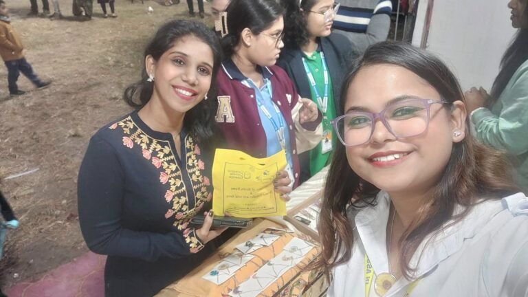Two smiling women at an outdoor market stall with handmade resin jewelry and keepsakes displayed on a table.