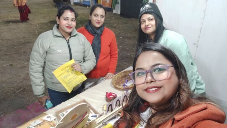 Four women smiling at a market stall with handmade resin keepsakes and decor displayed on a table.
