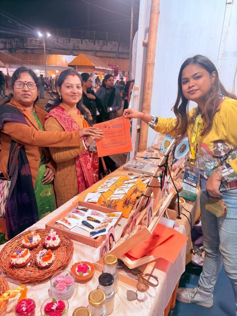 Three women at an evening market stall showcasing handmade resin jewelry, decorative hair clips, and various scented candles.