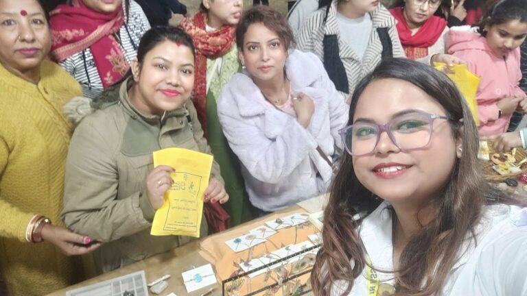 Smiling vendor in purple glasses takes a selfie at a market stall with customers browsing handmade resin jewelry and gifts.