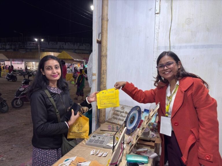 Two women smiling at a night market stall, one holding a yellow paper, the other a yellow bag, with handmade resin items on d