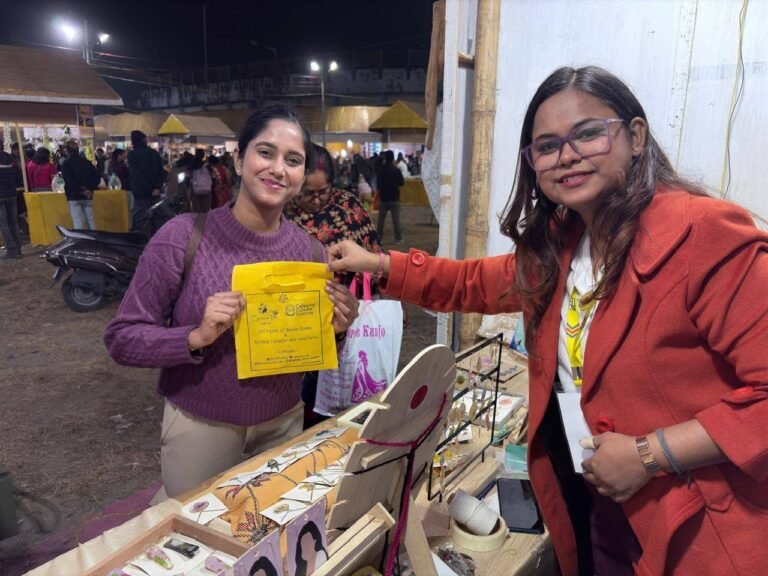 A smiling customer in a purple sweater receives a yellow shopping bag from a vendor at an outdoor market stall with resin jew