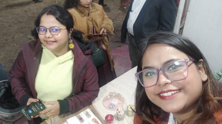 Two women smiling at a craft fair booth, showcasing handmade resin jewelry, decor, and scented candles on display.