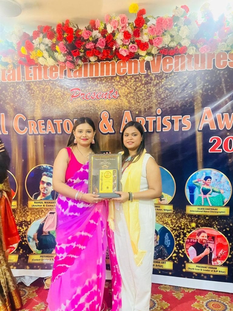 Two women, one in pink saree, one in white, holding a framed award at a Digital Creators & Artists Awards event.