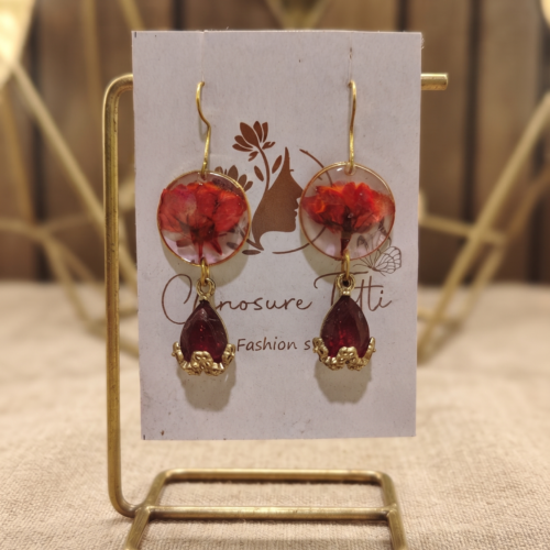 A pair of handcrafted gold-tone drop earrings featuring circular clear resin with preserved red flowers and deep red teardrop