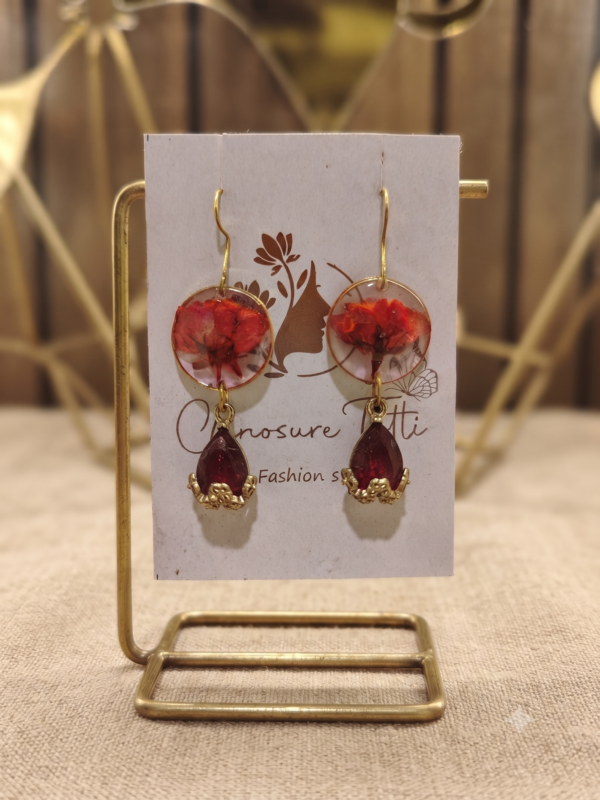 A pair of handcrafted gold-tone drop earrings featuring circular clear resin with preserved red flowers and deep red teardrop