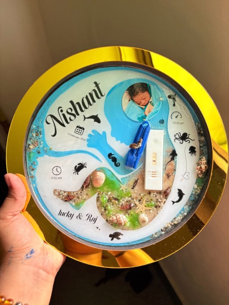 Handheld golden resin keepsake featuring baby Nishant's photo, birth details, umbilical clip, pregnancy test, and ocean eleme