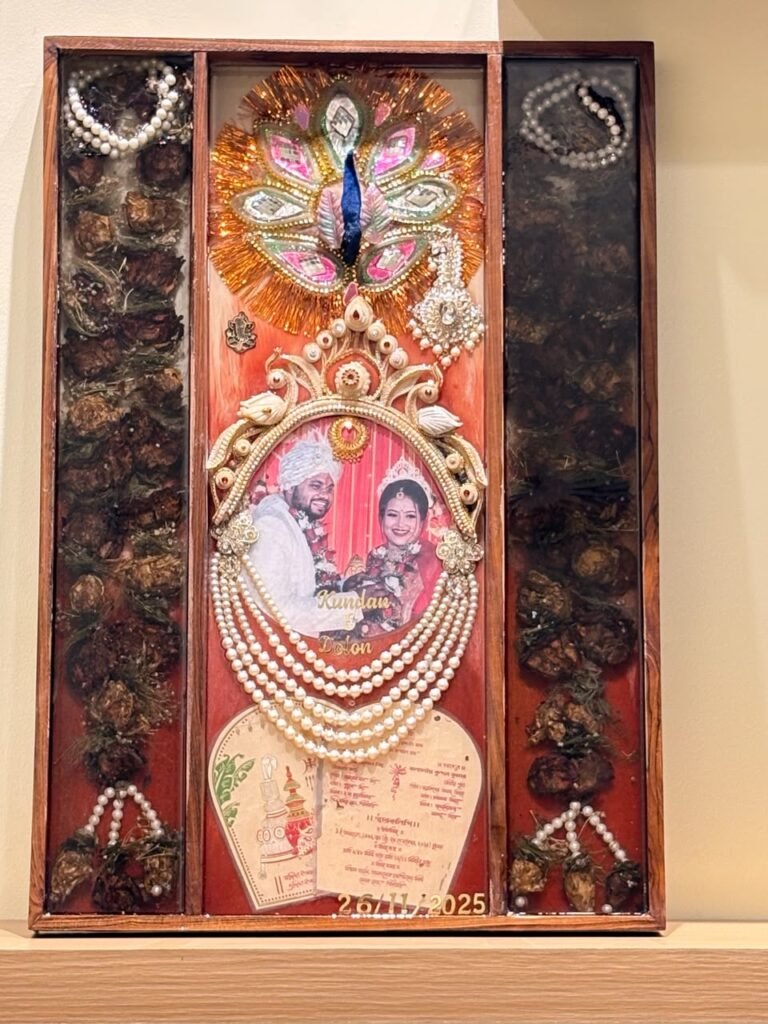 Ornate resin wedding keepsake featuring a couple's photo, peacock art, pearl garlands, invitation, and dried botanicals.