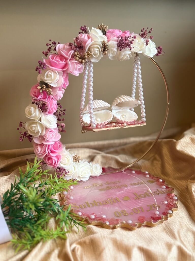 Personalized pink resin tray with names and date, featuring a floral arch and miniature swing with seashell cradles.