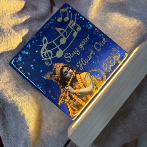 Blue resin keepsake featuring Krishna playing flute, golden musical notes, and 'Sing your Heart Out,' illuminated by a wooden