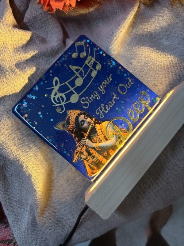Blue resin keepsake featuring Krishna playing flute, golden musical notes, and 'Sing your Heart Out,' illuminated by a wooden