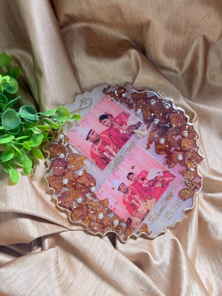 Personalized resin keepsake with two wedding photos, dried petals, gold flakes, and pearls on a golden fabric background.