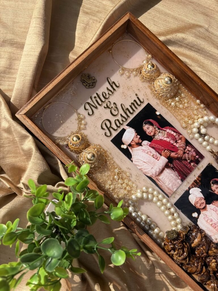 Personalized resin tray with gold names Nitesh & Rashmi, wedding photos, gold jhumkas, and pearl chains on a golden fabric.