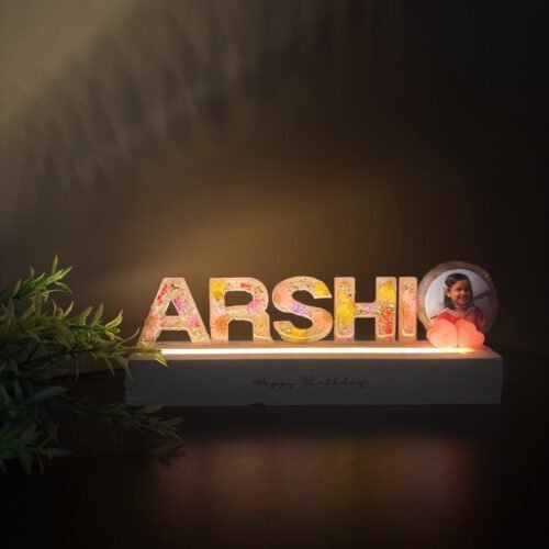 Illuminated resin nameplate "ARSHI" with colorful dried flowers, a child's photo, and glowing pink hearts on a "Happy Birthda